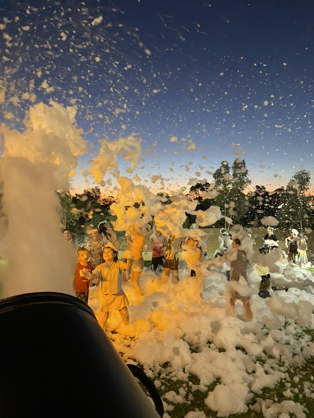 Children playing in foam at outdoor event during sunset